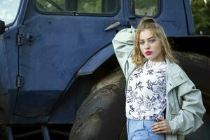 A beautiful country girl in the style of the 90s in bright clothes stands near a tractor. photo