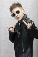 Portrait of a heavy metal boy in sunglasses. Cute teenager in a leather jacket doing a rock and roll sign photo