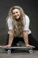 Beautiful fat woman with a skateboard on a gray background looks at the camera and smiles. photo