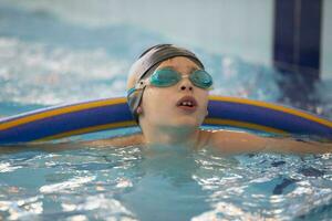 Boy in a swimming cap and swimming goggles in the pool. The child is engaged in the swimming section. photo