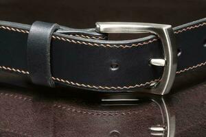 Black leather belt with a metal buckle on a dark background close-up. photo