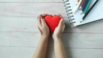 a woman's hands holding a red heart on a wooden table video