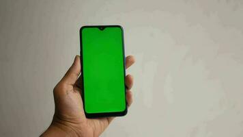 a hand holding a smartphone with a green screen video