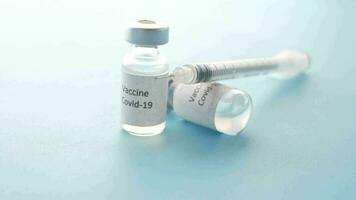 pequeño frasco de un vacuna y jeringuilla sentado en parte superior de un azul superficie video