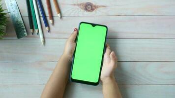 une femme main en portant une téléphone intelligent avec une vert écran sur une en bois table video
