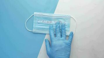 uma mão dentro azul luvas segurando uma cirúrgico mascarar com corona vírus escrito em isto video