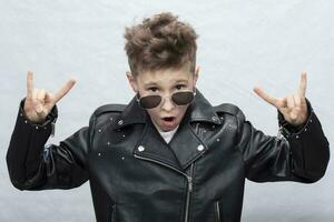 Portrait of a heavy metal boy in sunglasses. Cute teenager in a leather jacket doing a rock and roll sign photo