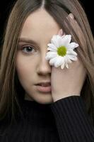 un hermosa niña con natural belleza sostiene un blanco flor cerca su ojo. joven niña con un blanco crisantemo. foto