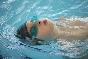 chico en un nadando gorra y nadando gafas de protección en el piscina. el niño es comprometido en el nadando sección. foto