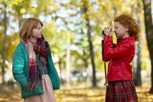 Two red-haired girls girlfriends photograph each other in the autumn park with a retro camera. photo