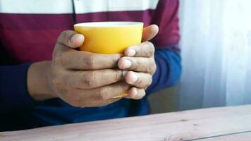 a man warm his hand by holding a yellow cup in his hands video