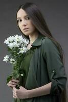 A beautiful young girl with natural beauty with long smooth hair holds a bouquet of white chrysanthemums. photo