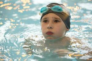 chico en un nadando gorra y nadando gafas de protección en el piscina. el niño es comprometido en el nadando sección. foto