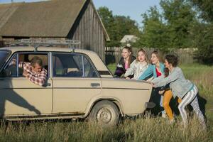 Young cheerful girls are pushing an old car. Women in the style of the 90s. photo