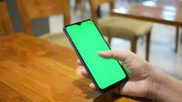 un hombre participación un teléfono inteligente con un verde pantalla en un restaurante video