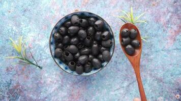 black olives in a bowl and a wooden spoon on a blue background video