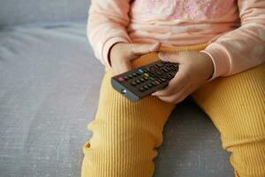 child holding tv remote while sitting on sofa photo