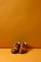 Pair of brown shoes sitting on top of wooden floor next to orange wall. Generative AI photo