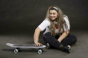 Beautiful plump woman with a skateboard on a gray background. photo
