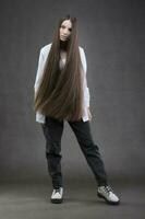 un hermosa niña con muy largo pelo en lleno crecimiento en un gris antecedentes. foto