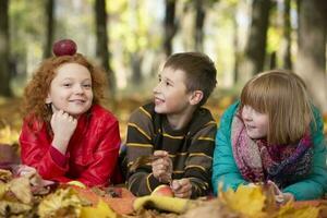 Two girls and a boy lie in the park in autumn leaves, communicate with each other. photo