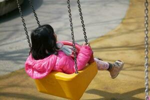 child having fun on a swing on the playground in public park. photo