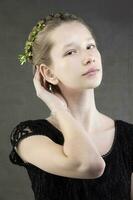 A beautiful teenage girl with a braid with a green twig of a tree woven into it on a gray background. Portrait of a pressed girl with sophisticated features. photo