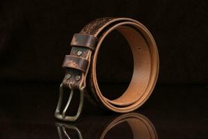 Brown leather belt with scuffs and a metal buckle on a dark background. photo