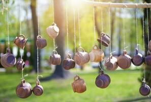 Clay cups hang from the ropes, illuminated by the sun. Sale of handicraft clay products. photo