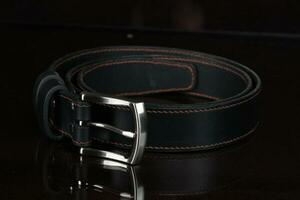 Black leather belt with a metal buckle on a dark background close-up. photo