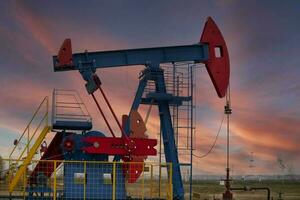 An oil rig pumps oil against the backdrop of a red sunset and a beautiful sky. photo