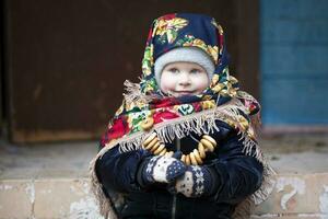 un pequeño niña en un ruso Pañuelo con Bagels a el maslenitsa día festivo. foto