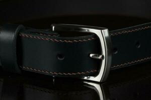 Black leather belt with a metal buckle on a dark background close-up. photo