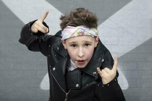 Portrait of a heavy metal boy in sunglasses. Cute teenager in a leather jacket doing a rock and roll sign photo