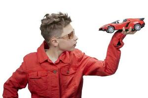 Fashionable boy holding a toy car in his hands, isolated on a white studio background. A handsome child dreaming of a real car. Dreams of a child about racing. photo