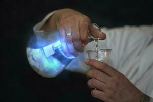 Chemical flask with a blue solution and a mystical glow in the hands of a laboratory assistant. Experiences and experiments. photo
