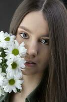 A beautiful young girl with natural beauty with long smooth hair holds a bouquet of white chrysanthemums. photo