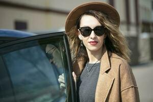 un hermosa niña en un beige elegante sombrero y Gafas de sol obtiene dentro el coche. Mujer francés. foto