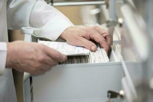 The nurse's hands are looking in the archive for a patient's card. The file is in a cell in the clinic. photo