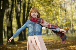 A red-haired girl in a warm scarf walks in the autumn park. photo