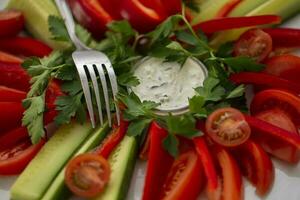 Sliced vegetables with sauce and a fork. Snack dish for a buffet table. photo