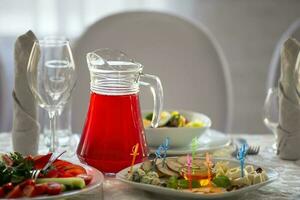 el comida es en el descansa en mesa. rojo compota en un vaso licorera y meriendas en el mesa. foto