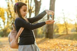 pequeño niña con reloj de arena rodeado por otoño follaje foto