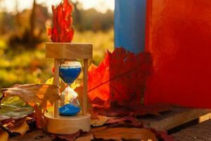 otoño hora tema, reloj de arena en caído hojas en varios colores con Copiar espacio. foto