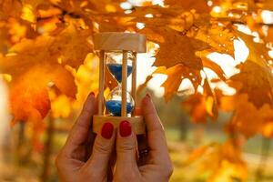 otoño hora tema, reloj de arena en caído hojas en varios colores con Copiar espacio. foto