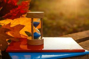 otoño hora tema, reloj de arena en caído hojas en varios colores con Copiar espacio. foto