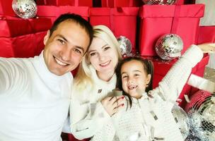 Christmas. Family. Technology. View on the smartphone. Dad, mom and daughter looking at camera and smiling while doing selfie photo