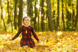 Very cheerful child having fun while tossing up yellow leaves photo