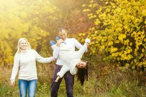 imagen de encantador familia en otoño parque, joven padres con bonito adorable hija jugando al aire libre, tener divertido en patio interior en caer, contento familia disfrutar otoñal naturaleza foto