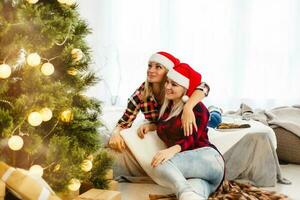 Close up lifestyle indoor portrait of two young woman posing near decorated Christmas tree, at New Year eve. Smiling having fun, ready for celebration. Bright holiday image of best friends. photo